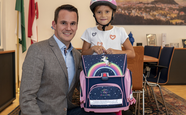 Foto von der Schultaschen-Übergabe: FPÖ-Klubobmann Stefan Hermann bei der Übergabe einer Schultasche an Sophia, die sich riesig darüber gefreut hat.